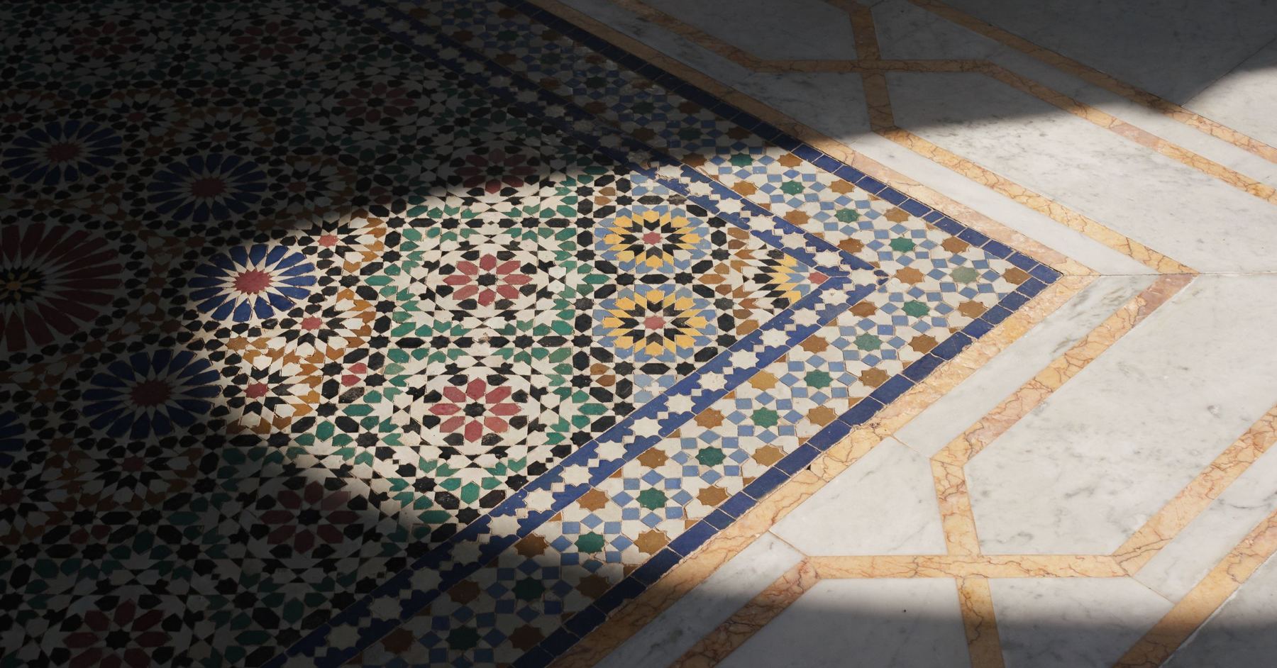 A geometric zellige mosaic floor in sunlight, bordered by pale marble